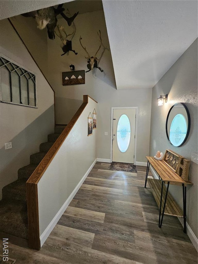 entryway with wood finished floors, stairway, baseboards, a textured ceiling, and lofted ceiling