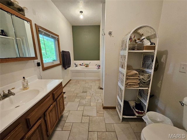 full bathroom with stone tile flooring, toilet, vanity, a garden tub, and baseboards