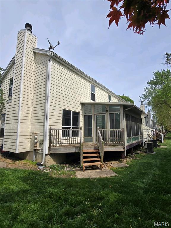 352 Sturbridge Village Dr, Hazelwood, MO 63042 - back of property featuring a sunroom, a chimney, central AC unit, a yard, and a wooden deck