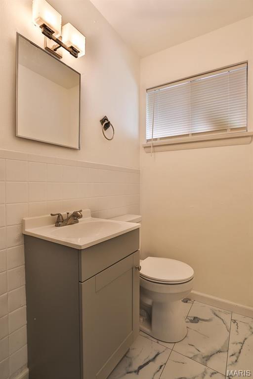 4417 Wallace St, Saint Louis, MO 63116 - bathroom with marble look tiles, vanity, toilet, a wainscoted wall, and tile walls