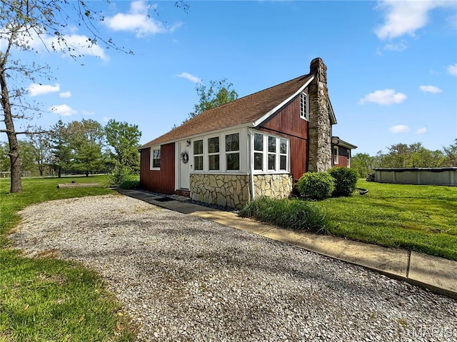 view of side of home with a yard, stone siding, and a chimney