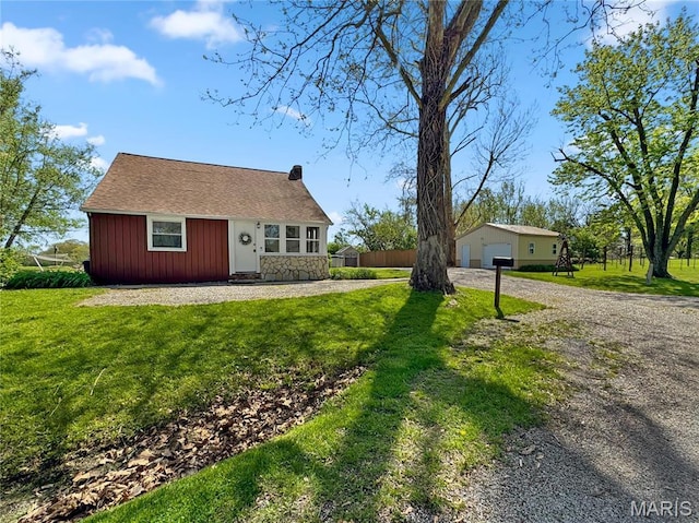 view of front facade with an outbuilding, a front yard, a chimney, driveway, and stone siding