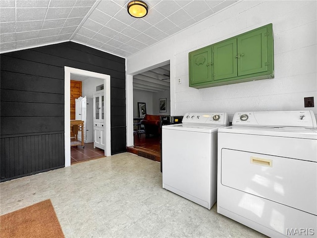 washroom with washing machine and dryer, cabinet space, wooden walls, and light floors