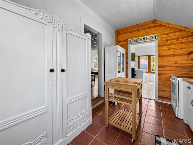 dining room with lofted ceiling, wood walls, and dark tile patterned floors