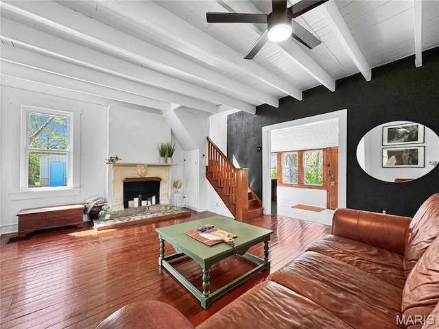 living area featuring stairway, wood-type flooring, ceiling fan, healthy amount of natural light, and beamed ceiling