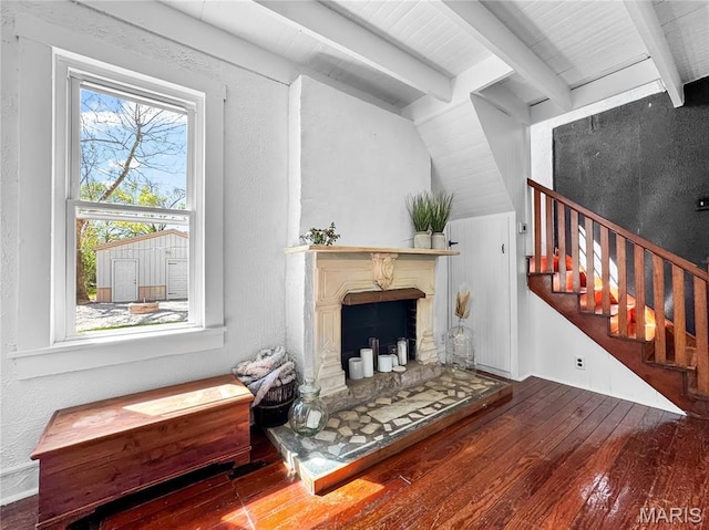 living room with wood-type flooring, stairs, a fireplace with raised hearth, and a textured wall
