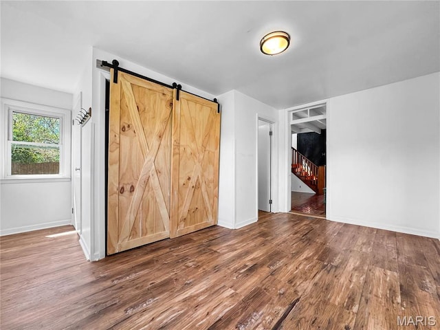 unfurnished room with a barn door, wood finished floors, baseboards, and stairs