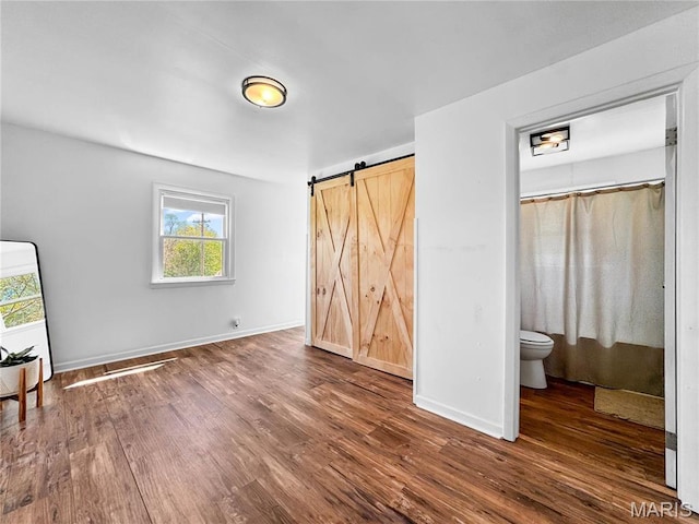 unfurnished bedroom featuring wood finished floors, a barn door, and baseboards