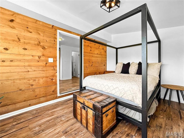 bedroom with baseboards, wood finished floors, and wood walls