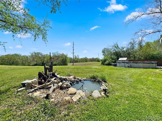 view of green lawn featuring a small pond and a covered pool