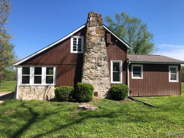 view of side of home featuring stone siding, a chimney, and a yard