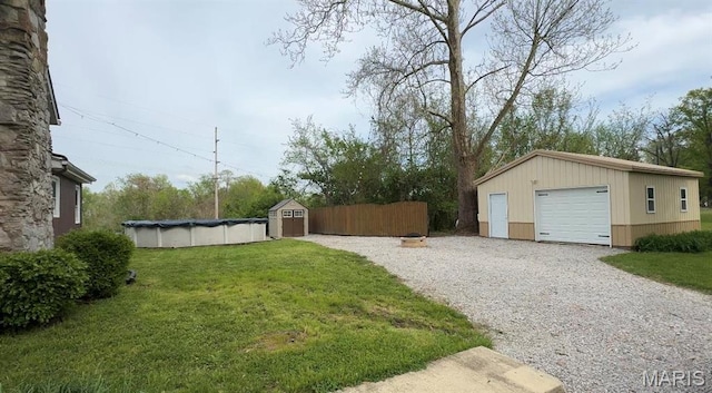 view of grassy yard with an outdoor structure, gravel driveway, a garage, and a covered pool