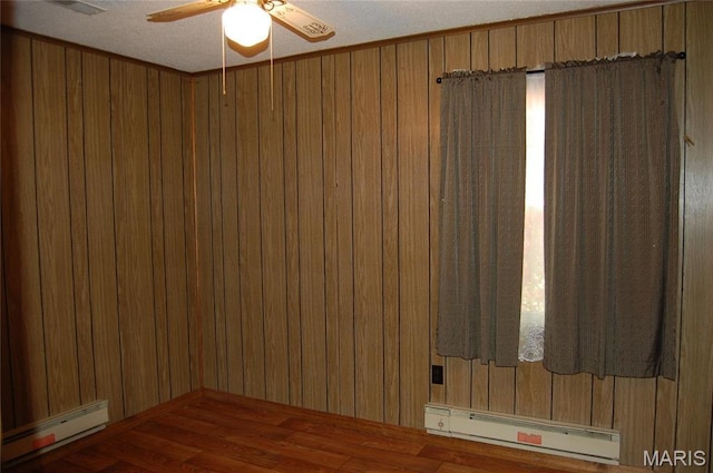 unfurnished room featuring baseboard heating, a baseboard radiator, wood finished floors, a ceiling fan, and wood walls