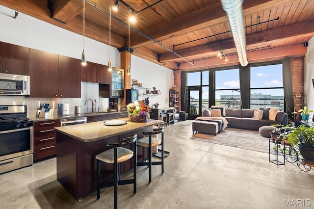 kitchen with appliances with stainless steel finishes, wood ceiling, a breakfast bar area, finished concrete floors, and beamed ceiling