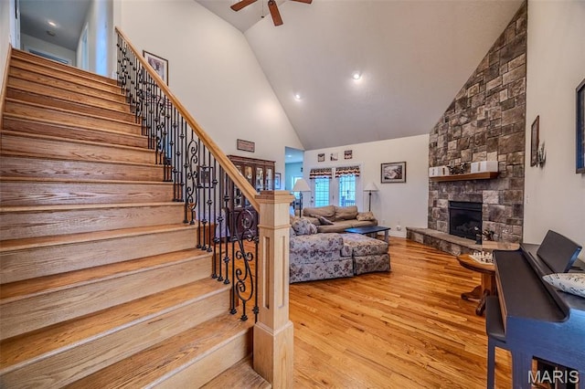 living area featuring high vaulted ceiling, a ceiling fan, stairway, wood finished floors, and a fireplace