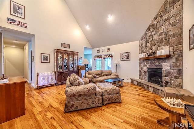 living room featuring high vaulted ceiling, light wood-style floors, a fireplace, and baseboards