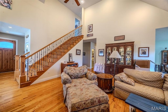 living area featuring high vaulted ceiling, a ceiling fan, stairway, wood finished floors, and baseboards