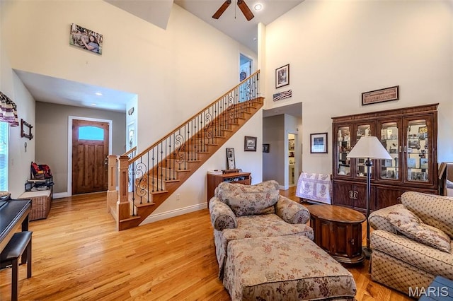 living area featuring stairs, a towering ceiling, ceiling fan, wood finished floors, and baseboards
