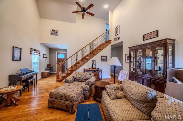living area with a high ceiling, stairway, ceiling fan, wood finished floors, and baseboards