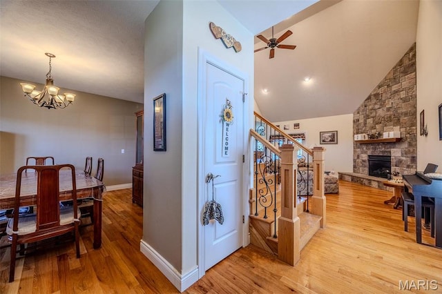 corridor featuring light wood finished floors, stairway, a chandelier, baseboards, and high vaulted ceiling