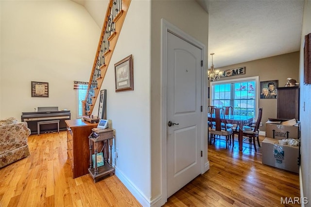 corridor with a chandelier, light wood-style floors, and baseboards