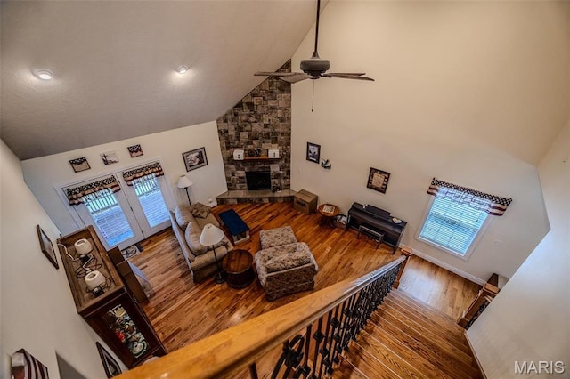 living area featuring high vaulted ceiling, a ceiling fan, wood finished floors, healthy amount of natural light, and a stone fireplace