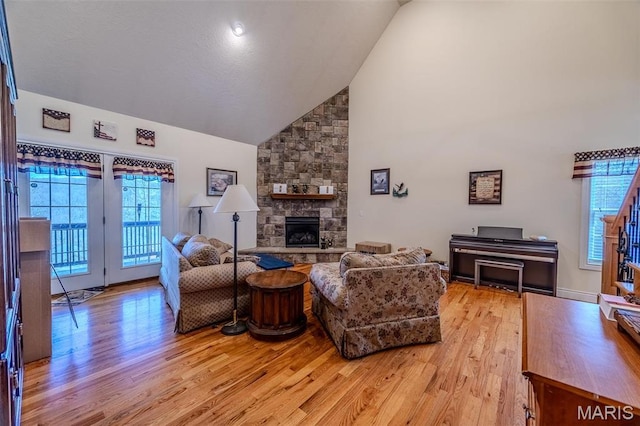 living area with light wood-style flooring, a fireplace, and high vaulted ceiling