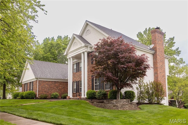 neoclassical home featuring a front yard, a chimney, brick siding, and an attached garage