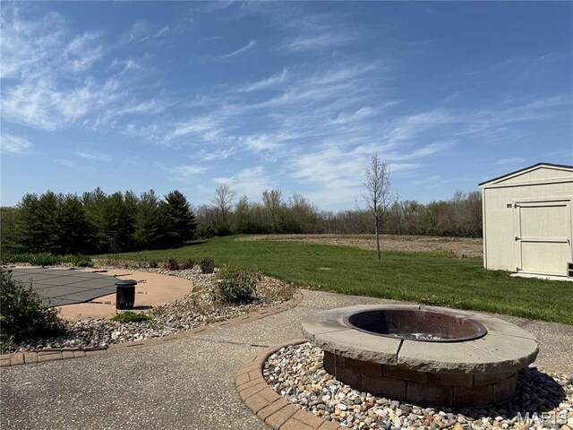 view of green lawn featuring a storage unit, a fire pit, and an outbuilding