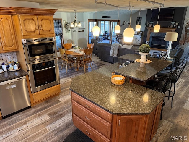 kitchen with appliances with stainless steel finishes, open floor plan, dark wood-style flooring, a kitchen island with sink, and brown cabinets