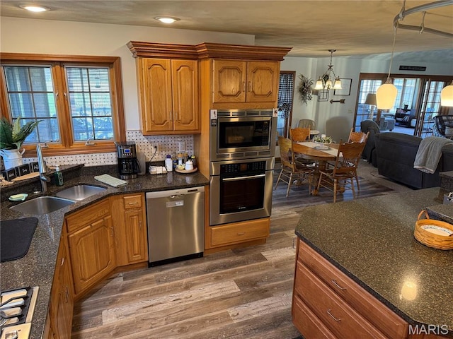 kitchen with appliances with stainless steel finishes, a sink, wood finished floors, a chandelier, and brown cabinetry