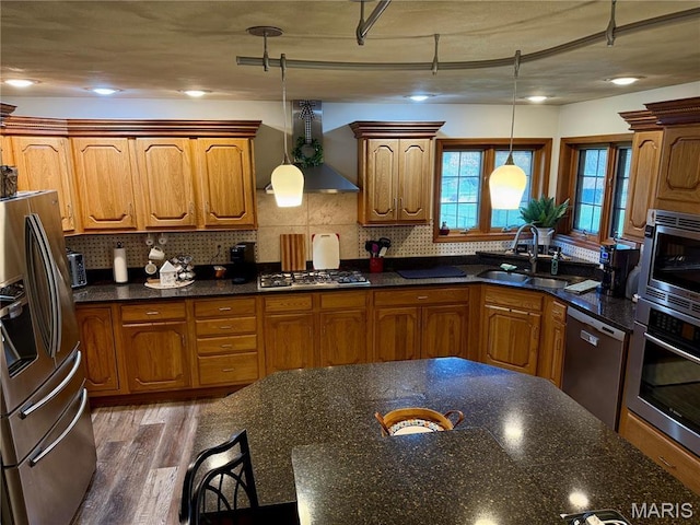 kitchen with appliances with stainless steel finishes, a sink, wall chimney exhaust hood, and brown cabinets