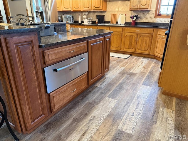 kitchen featuring a warming drawer, light wood finished floors, decorative backsplash, and brown cabinetry
