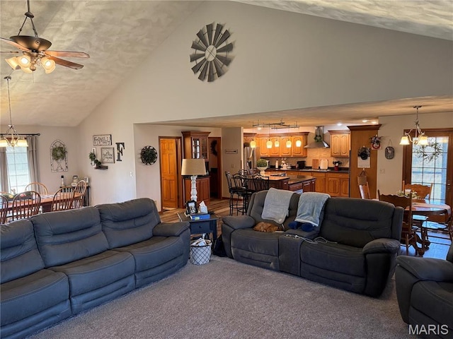 living area with a chandelier, light colored carpet, a textured ceiling, high vaulted ceiling, and a ceiling fan