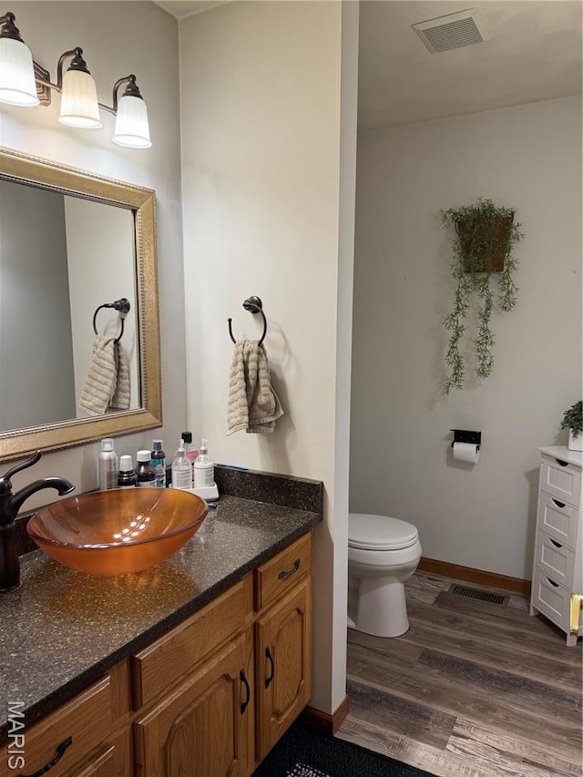 bathroom with wood finished floors, toilet, vanity, and baseboards