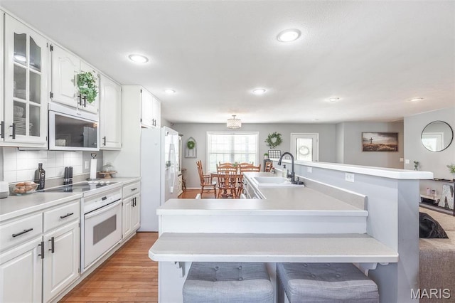kitchen featuring oven, a sink, black electric stovetop, recessed lighting, and light wood-style floors