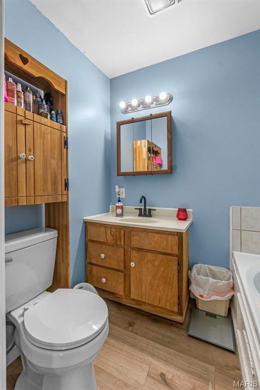 bathroom featuring wood finished floors, toilet, vanity, and a tub