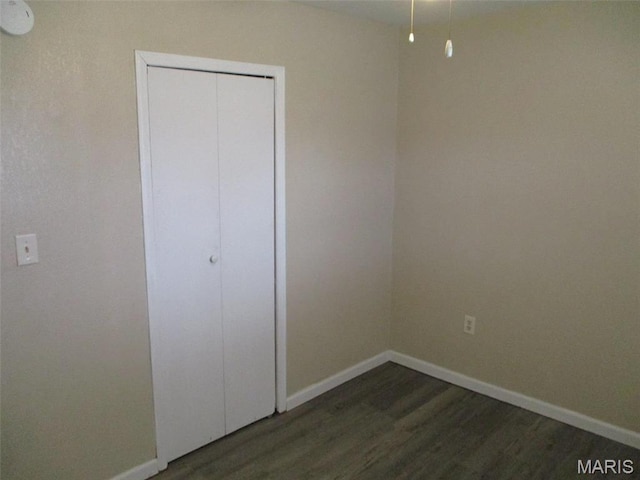 unfurnished bedroom with dark wood-style flooring, baseboards, and a closet