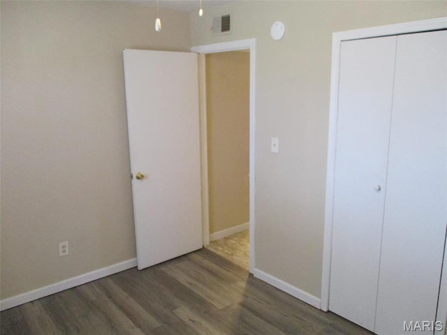 unfurnished bedroom with wood finished floors, baseboards, and a closet
