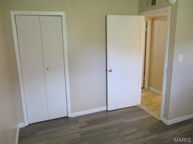 unfurnished bedroom with wood finished floors, baseboards, and a closet