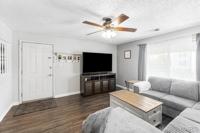 living room featuring dark wood-style flooring, ceiling fan, baseboards, and a textured ceiling