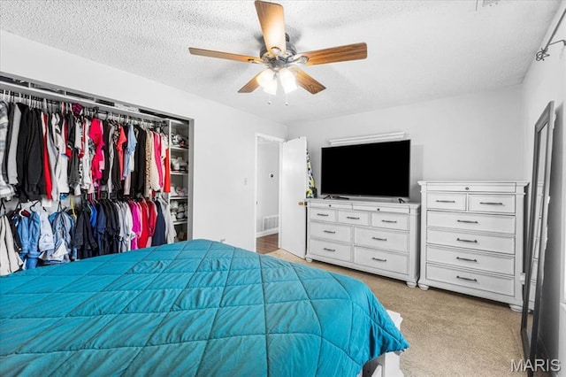 bedroom with a textured ceiling, a closet, light colored carpet, and ceiling fan