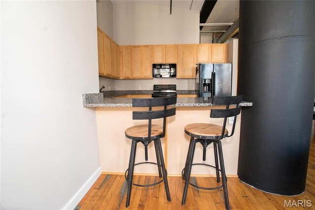 1520 Washington Ave Unit 604, Saint Louis, MO 63103 - kitchen featuring black appliances, light brown cabinets, light wood finished floors, a breakfast bar, and a peninsula
