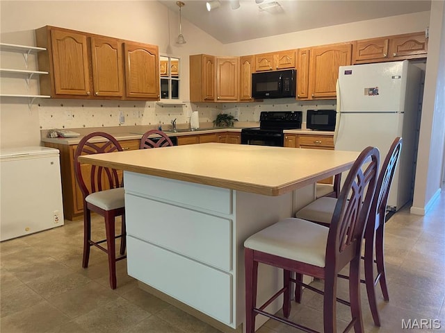 kitchen featuring black appliances, lofted ceiling, a kitchen island, a breakfast bar, and light countertops