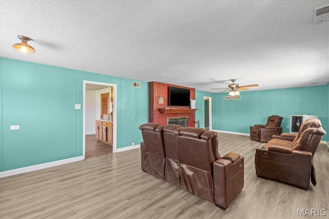 living room featuring wood finished floors, a textured ceiling, a brick fireplace, a ceiling fan, and baseboards