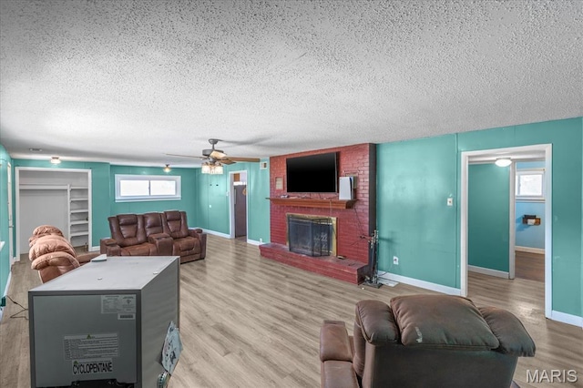 living area with a textured ceiling, a fireplace, a ceiling fan, light wood-style flooring, and baseboards
