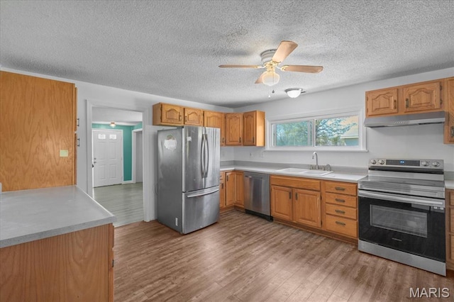 kitchen featuring appliances with stainless steel finishes, a sink, under cabinet range hood, ceiling fan, and wood finished floors