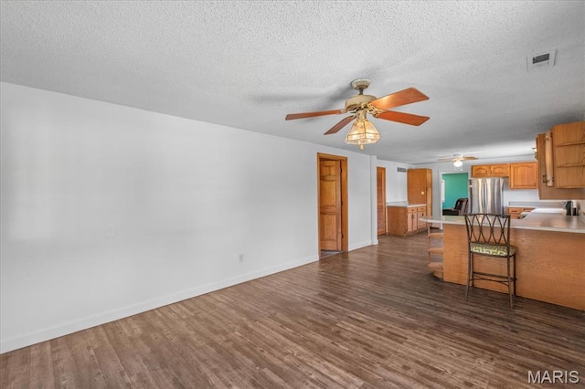 kitchen featuring freestanding refrigerator, ceiling fan, dark wood-style floors, light countertops, and a peninsula