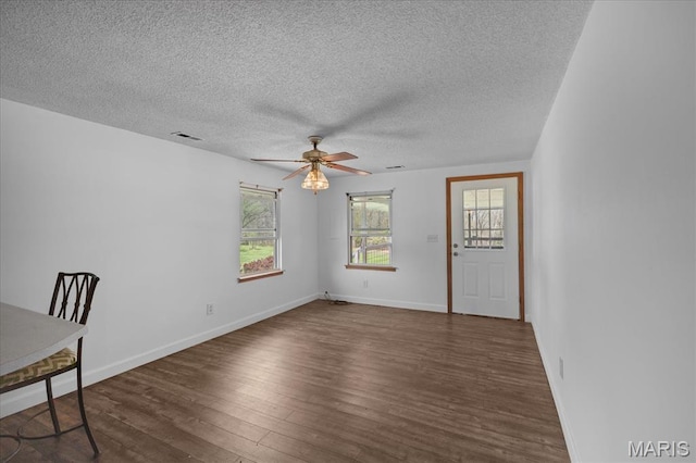 unfurnished dining area featuring a ceiling fan, dark wood-style floors, a textured ceiling, and baseboards
