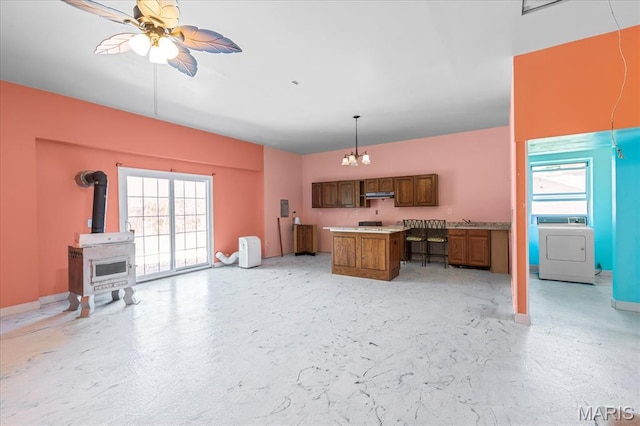 kitchen featuring washer / dryer, brown cabinetry, open floor plan, a wood stove, and healthy amount of natural light
